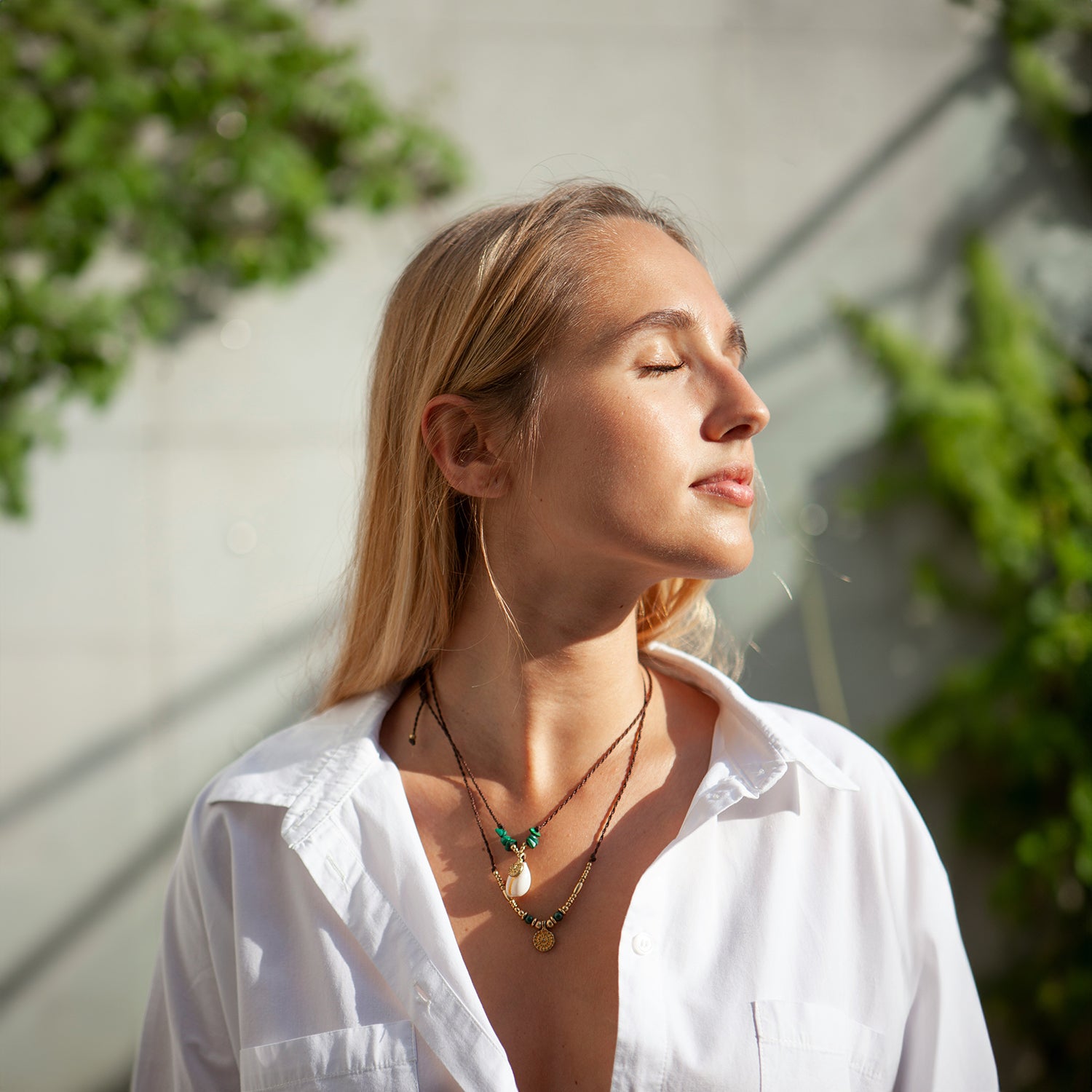 Beautiful woman with eyes closed basking in the sun open white shirt necklaces long blond hair