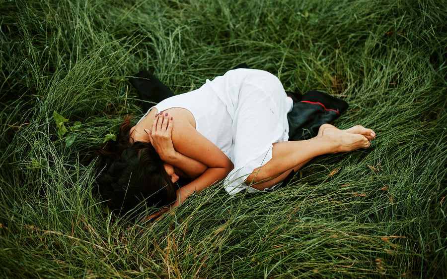Woman in white dress curled up on green grass, hands covering face