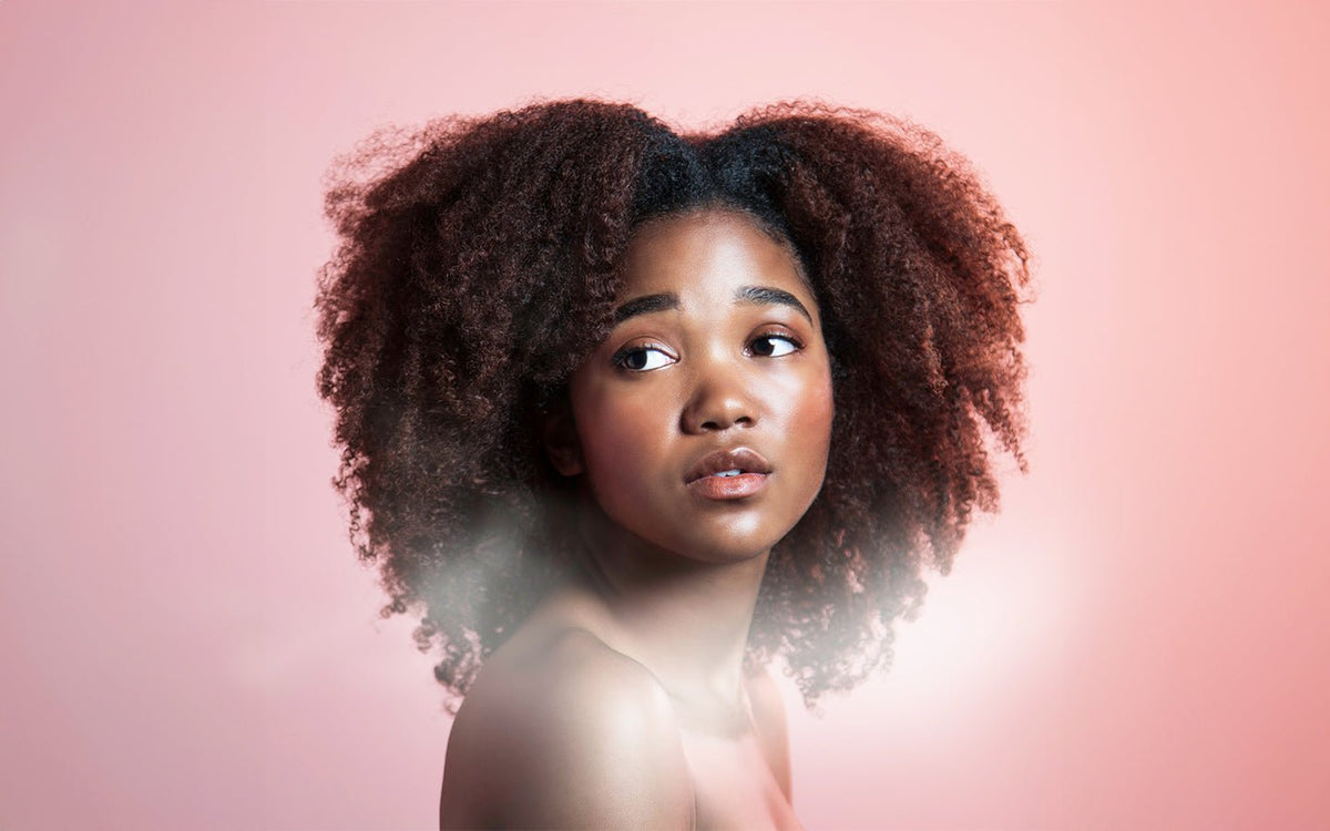 Young Black woman with natural hair looking left on a pink background