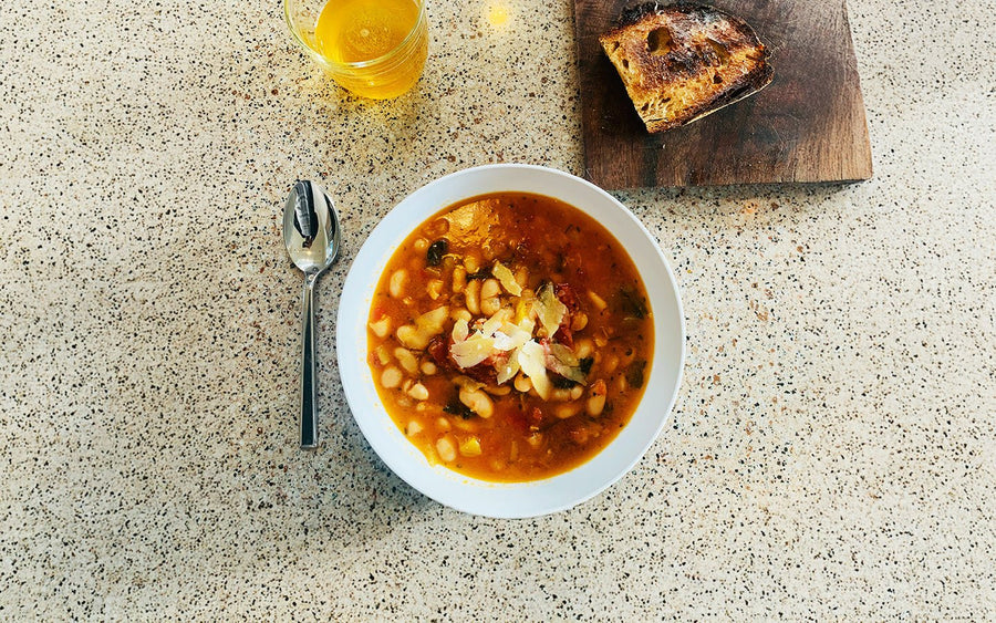 White bean soup with parmesan, spoon, drink, and toasted bread on a speckled counter