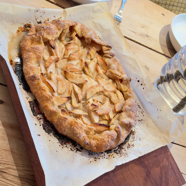 Apple galette with golden crust on parchment paper atop a wooden serving board.