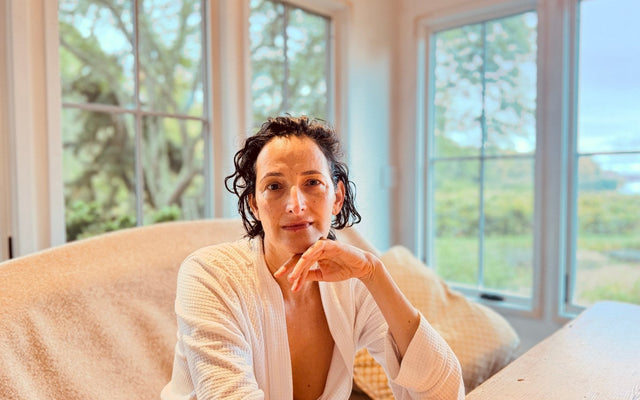 Dr. Catherine at home in a white robe, seated beside large windows.