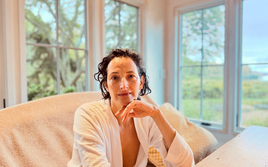 Dr. Catherine at home in a white robe, seated beside large windows.