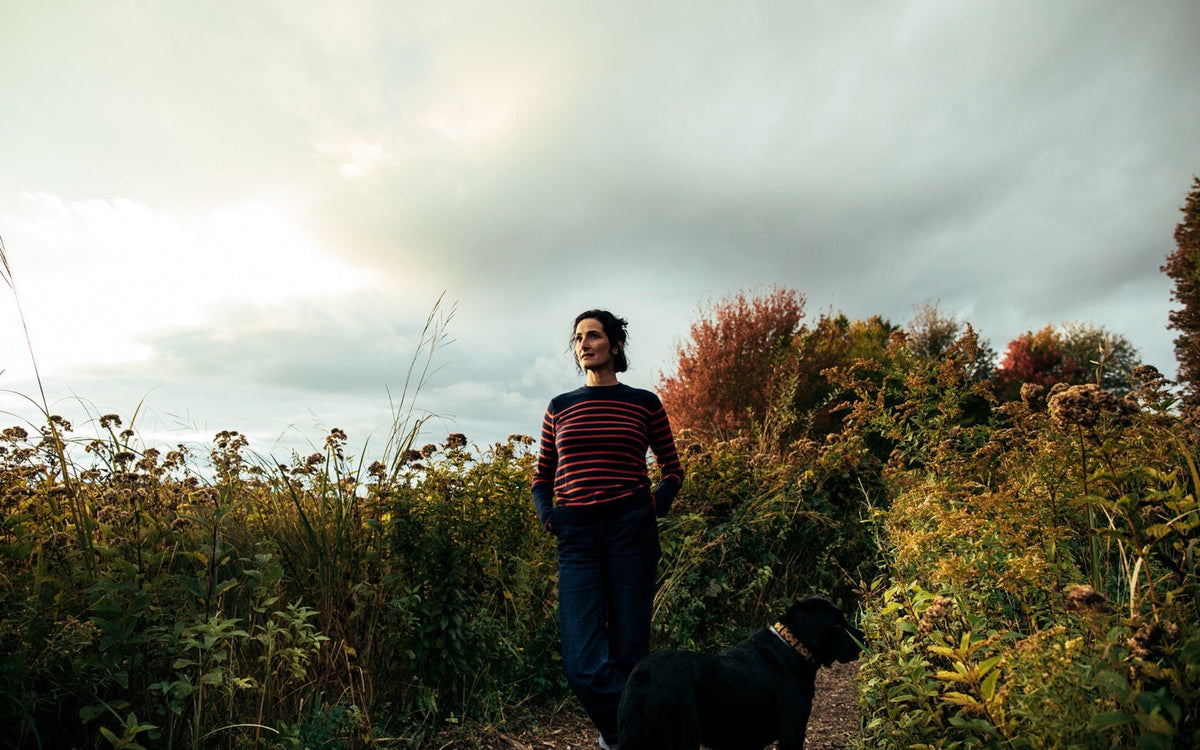 Dr. Catherine standing with a black dog on a path among autumn plants beneath a cloudy sky.