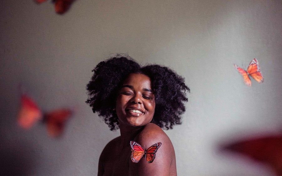 Smiling woman with dark curly hair and a monarch butterfly on her shoulder
