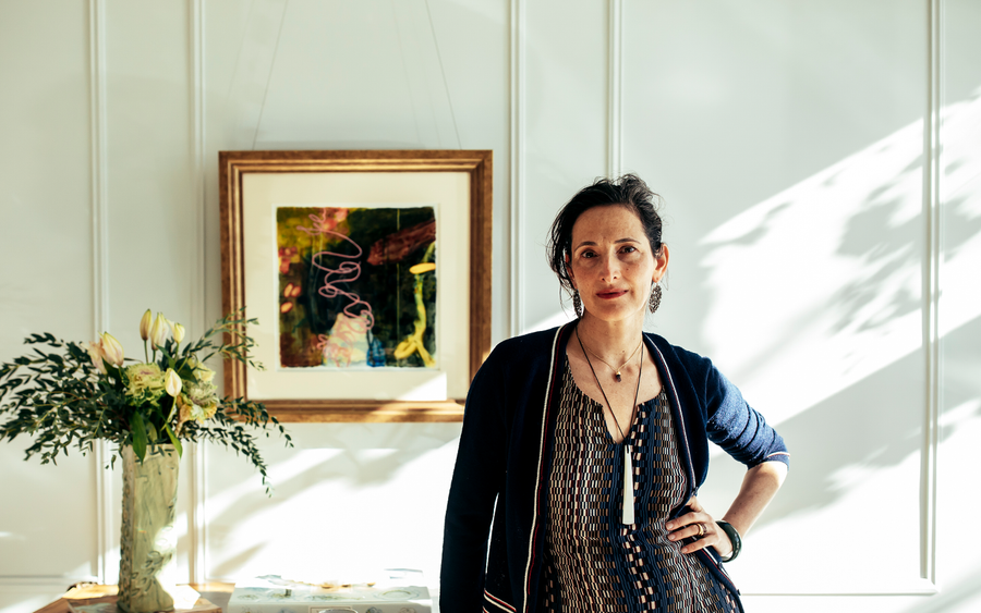 Dr. Catherine in a sunlit white-panelled room, a long pale pendant resting over her heart
