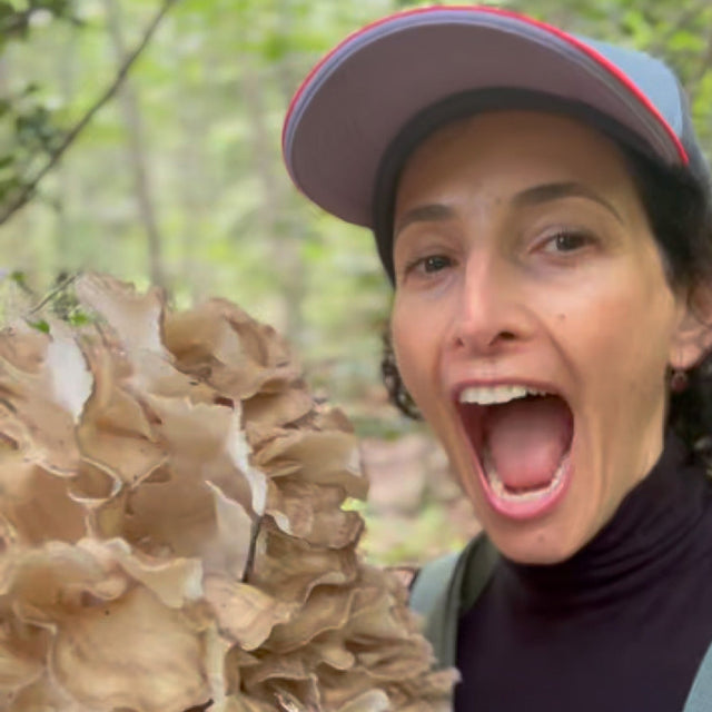 Dr. Catherine smiling beside a large cluster of mushrooms while foraging outdoors.