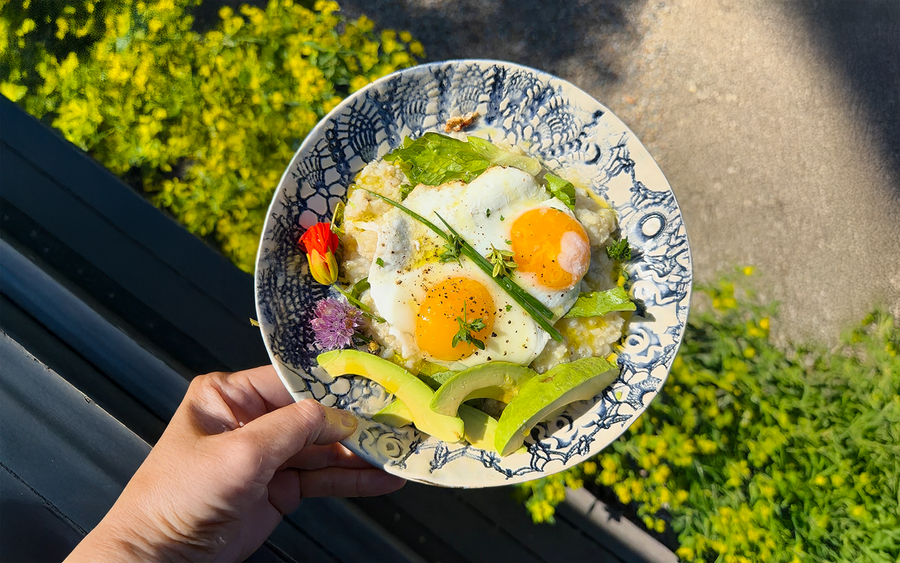 Dr. Catherine's savory millet porridge bowl topped with eggs, avocado, chives, and nasturtium held outdoors in morning light