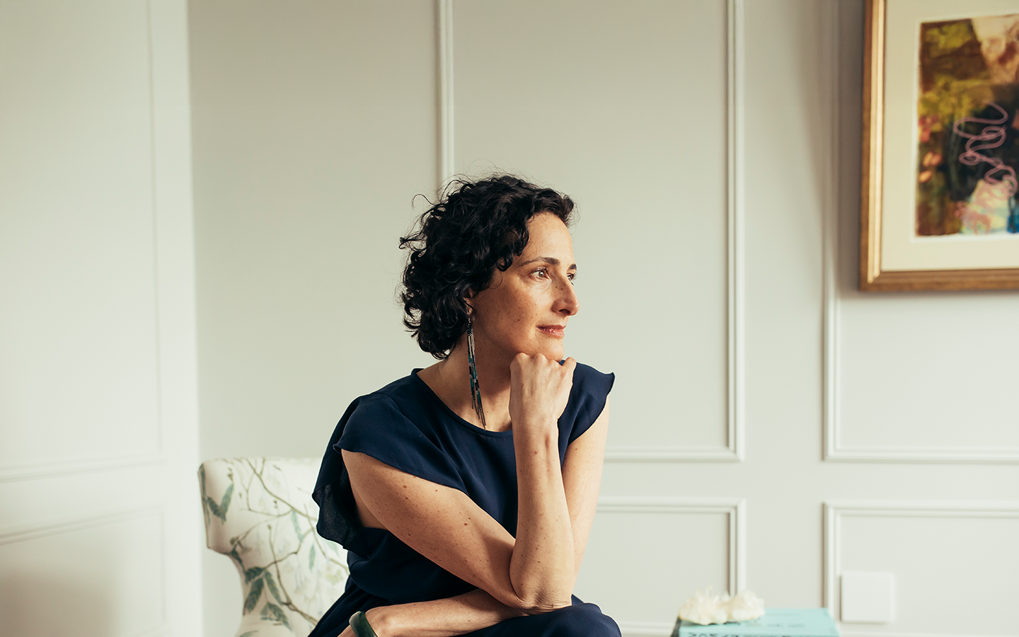 Dr. Catherine gazing toward the window in quiet reflection, chin resting on her hand