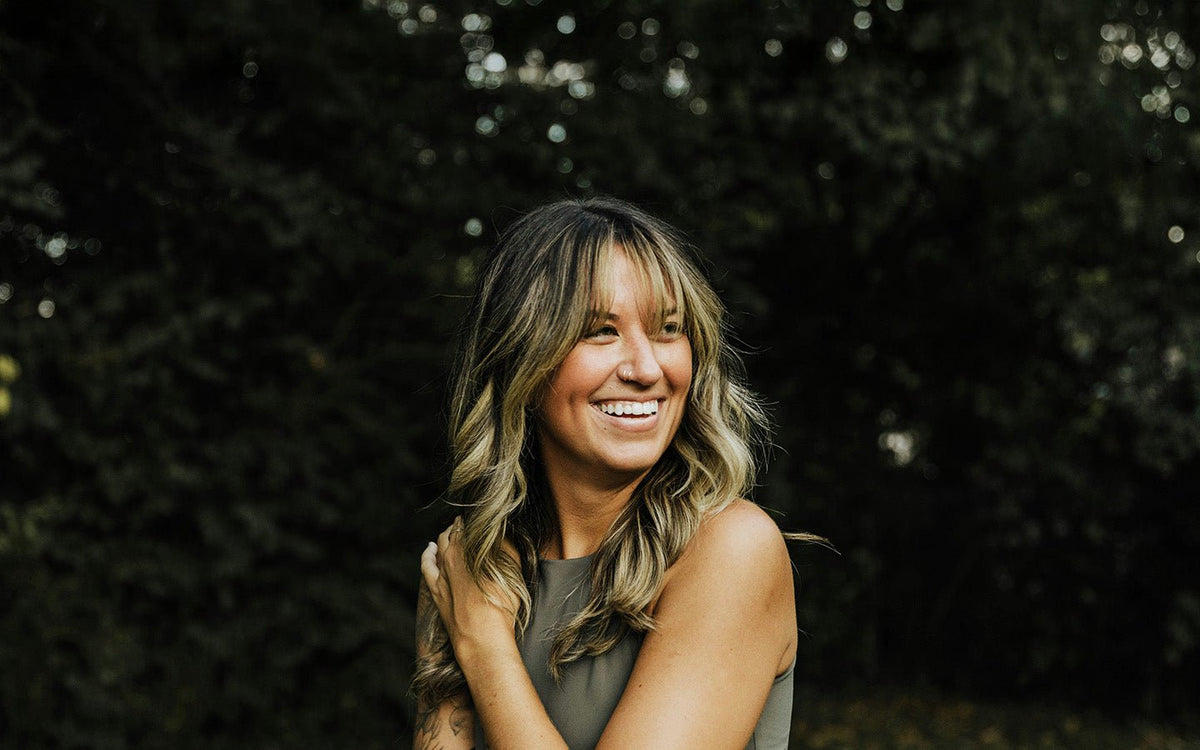 Smiling woman with blonde hair and nose ring in a green top against a dark green background