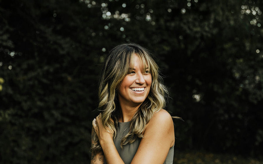 Smiling woman with blonde hair and nose ring in a green top against a dark green background