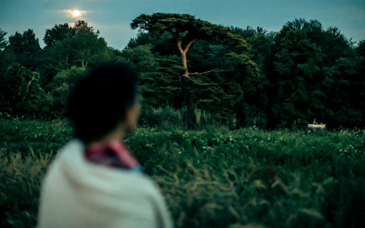 Dr. Catherine seen from behind, looking toward trees beneath a glowing moon.