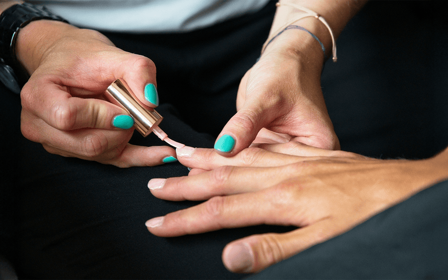 Manicurist applying light pink nail polish to a client's fingernails