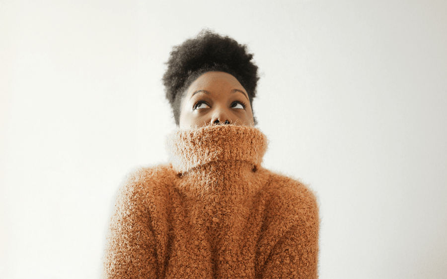 Woman in a fuzzy brown turtleneck looking up against a white background