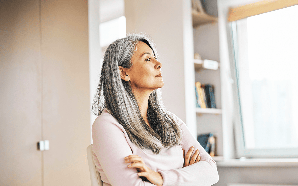 Confident woman with silver hair gazing thoughtfully by a sunlit window