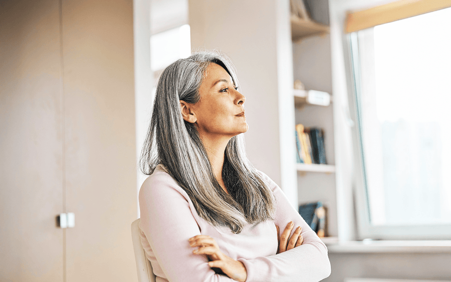 Confident woman with silver hair gazing thoughtfully by a sunlit window
