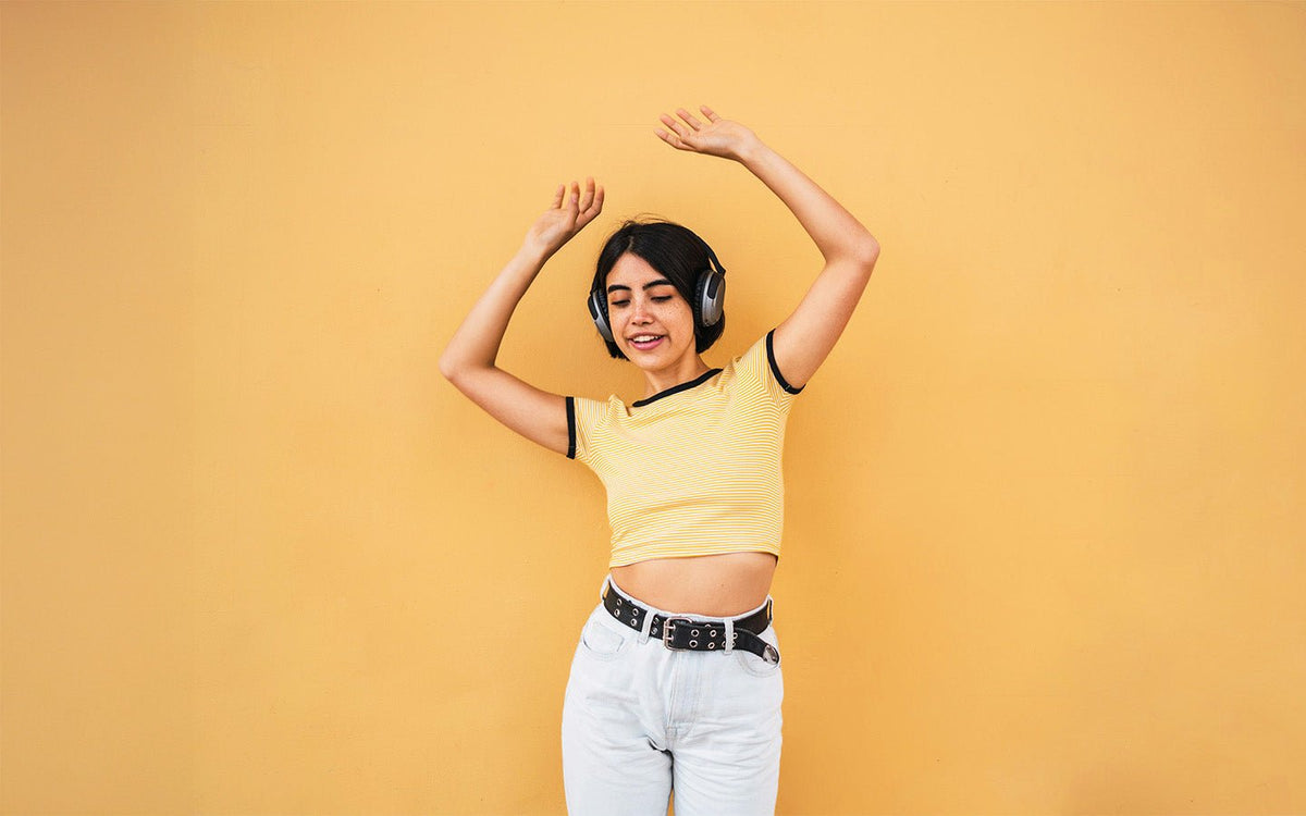 Young woman with headphones dancing against a yellow wall