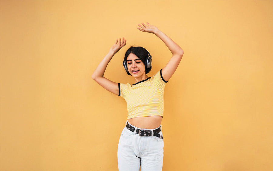 Young woman with headphones dancing against a yellow wall