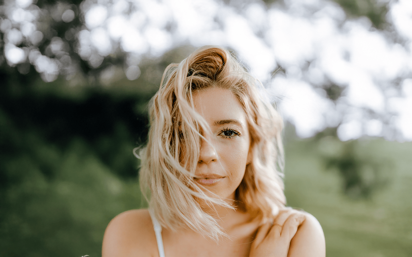 Radiant woman outdoors with natural windblown hair against a backdrop of trees