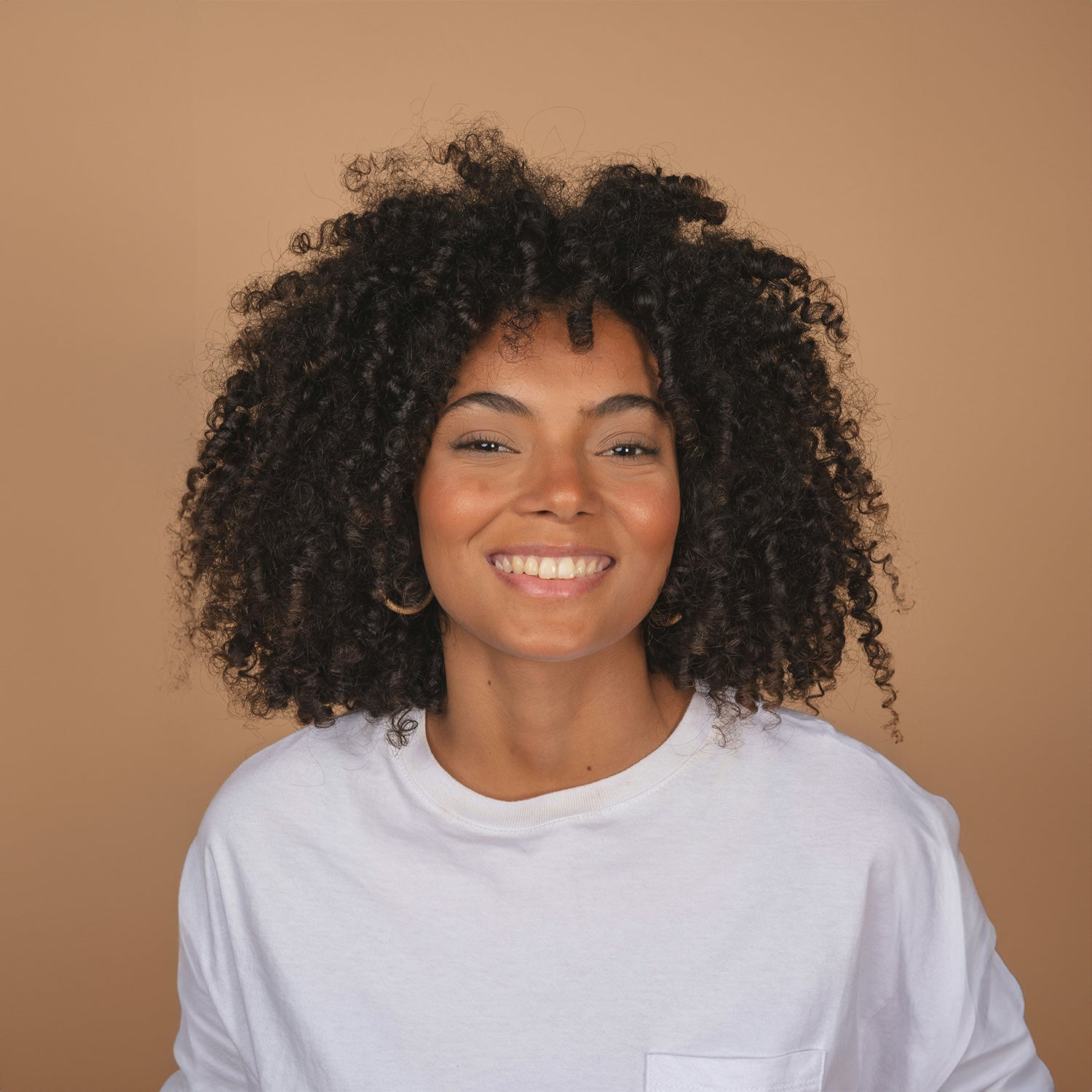 Smiling brown skin woman lots of curly hair in loose white t-shirt